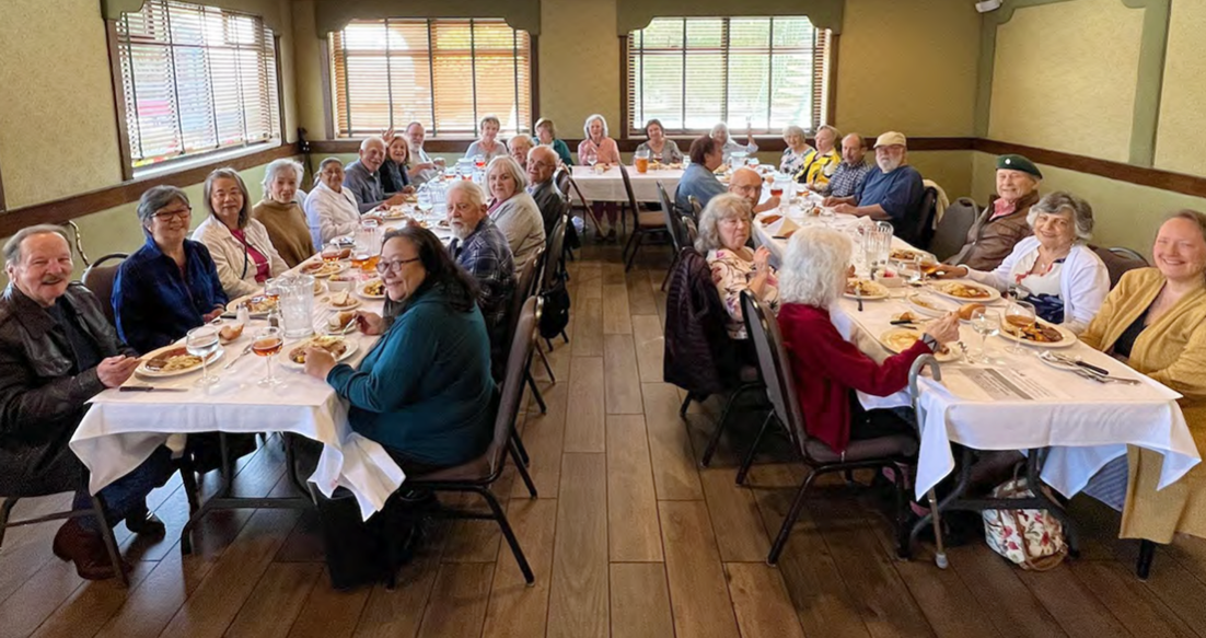 Large group of older adults sitting and enjoying community meal.